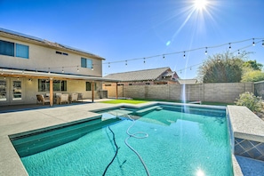 A swimming pool with a hose, a patio with chairs, and a building with a tiled roof.