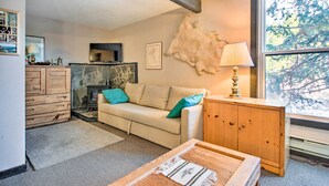 A cozy living room with a sofa, wooden cabinet, and a large window with a view of trees. - Cozy Big Sky Studio ~ 1 Mile to Mtn Village! (Big Sky)
