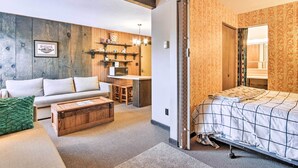 A modern living room with a sofa, coffee table, and a kitchen area with wooden shelves. - Cozy Big Sky Studio ~ 1 Mile to Mtn Village! (Big Sky)