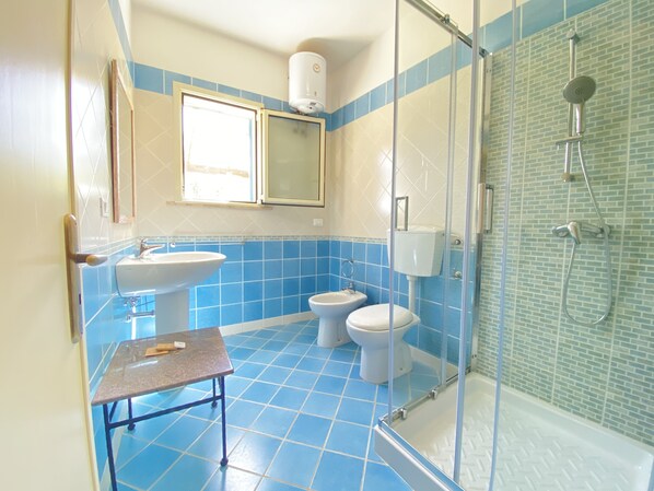 Une salle de bain avec des carreaux bleus et blancs, un lavabo, des toilettes, un espace douche et une fenêtre.