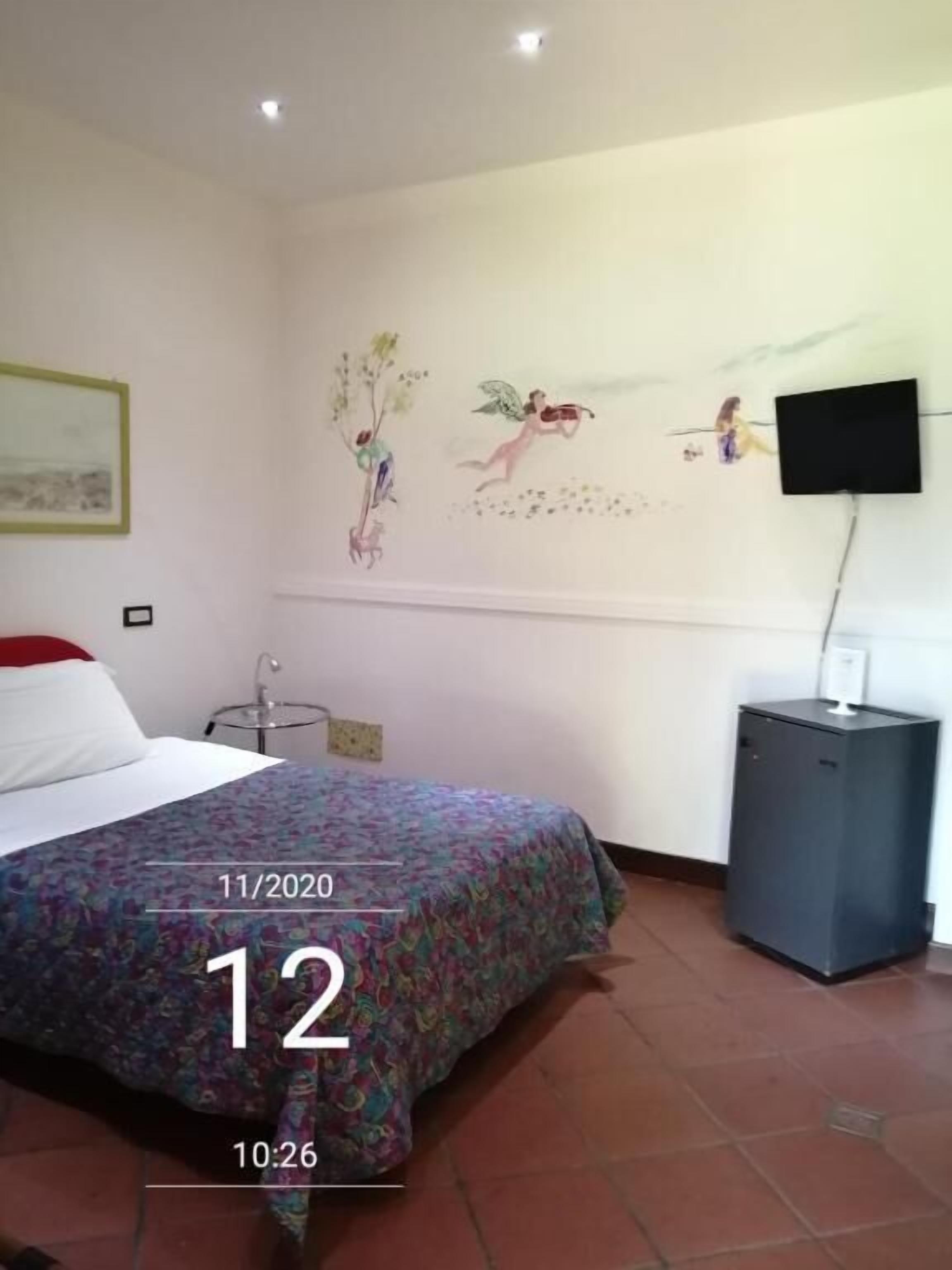 A hotel room with a bed, a television, a small cabinet, and wall art.