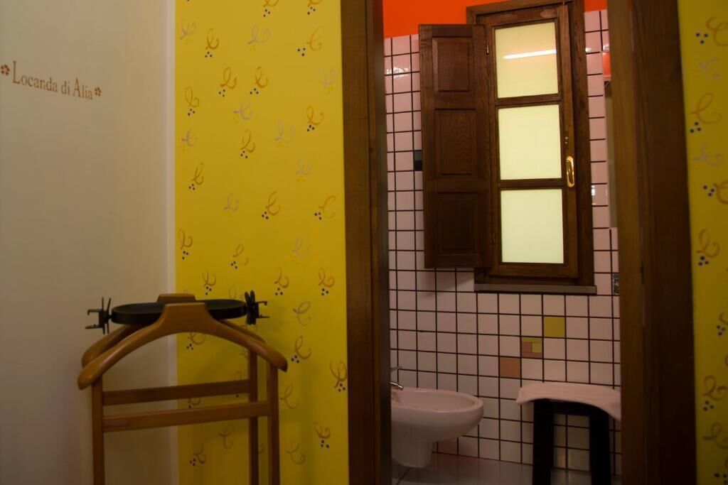 Une salle de bain avec un mur jaune, une porte en bois, un lavabo blanc et des toilettes.