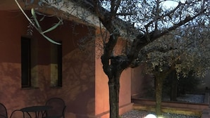 An outdoor seating area with a table and chairs, a tree, and a light source on the ground. - Gaia B&b (Castrovillari)