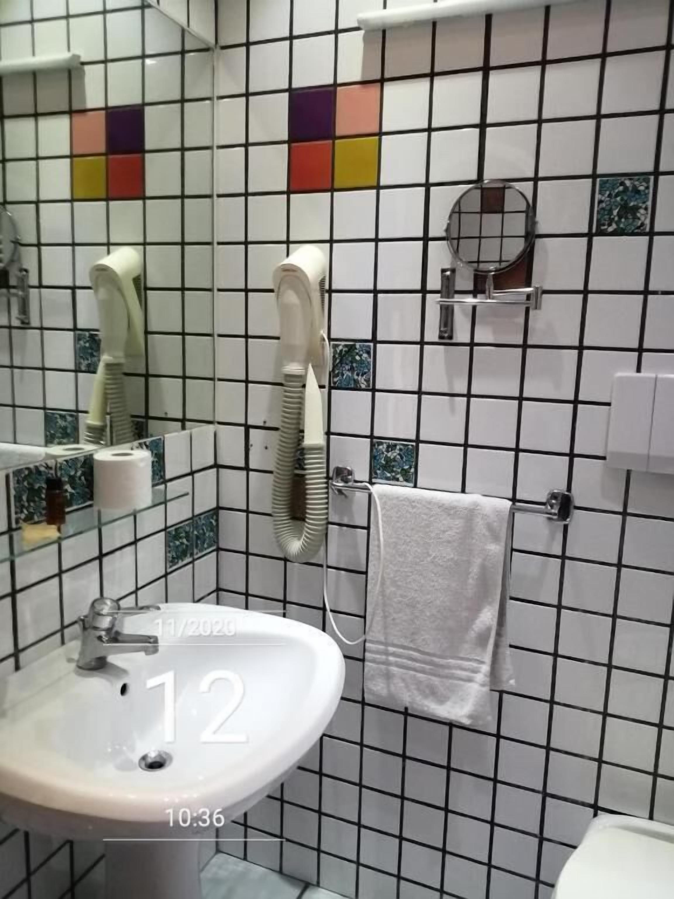 Een badkamer met een witte wasbak, een spiegel, een handdoekhouder en een haardroger.