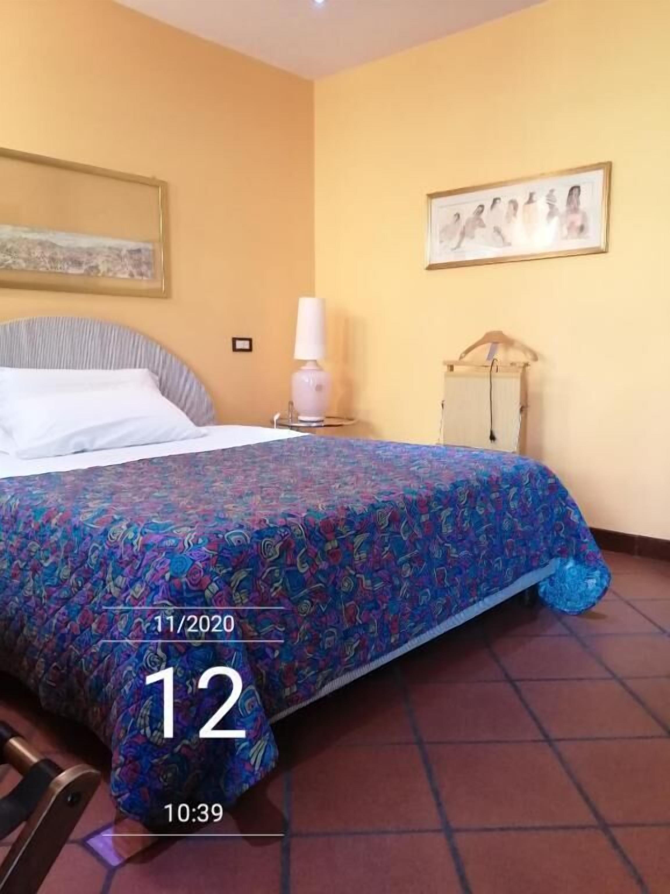 A hotel room with a bed, a nightstand, a lamp, a wardrobe, and a painting on the wall.