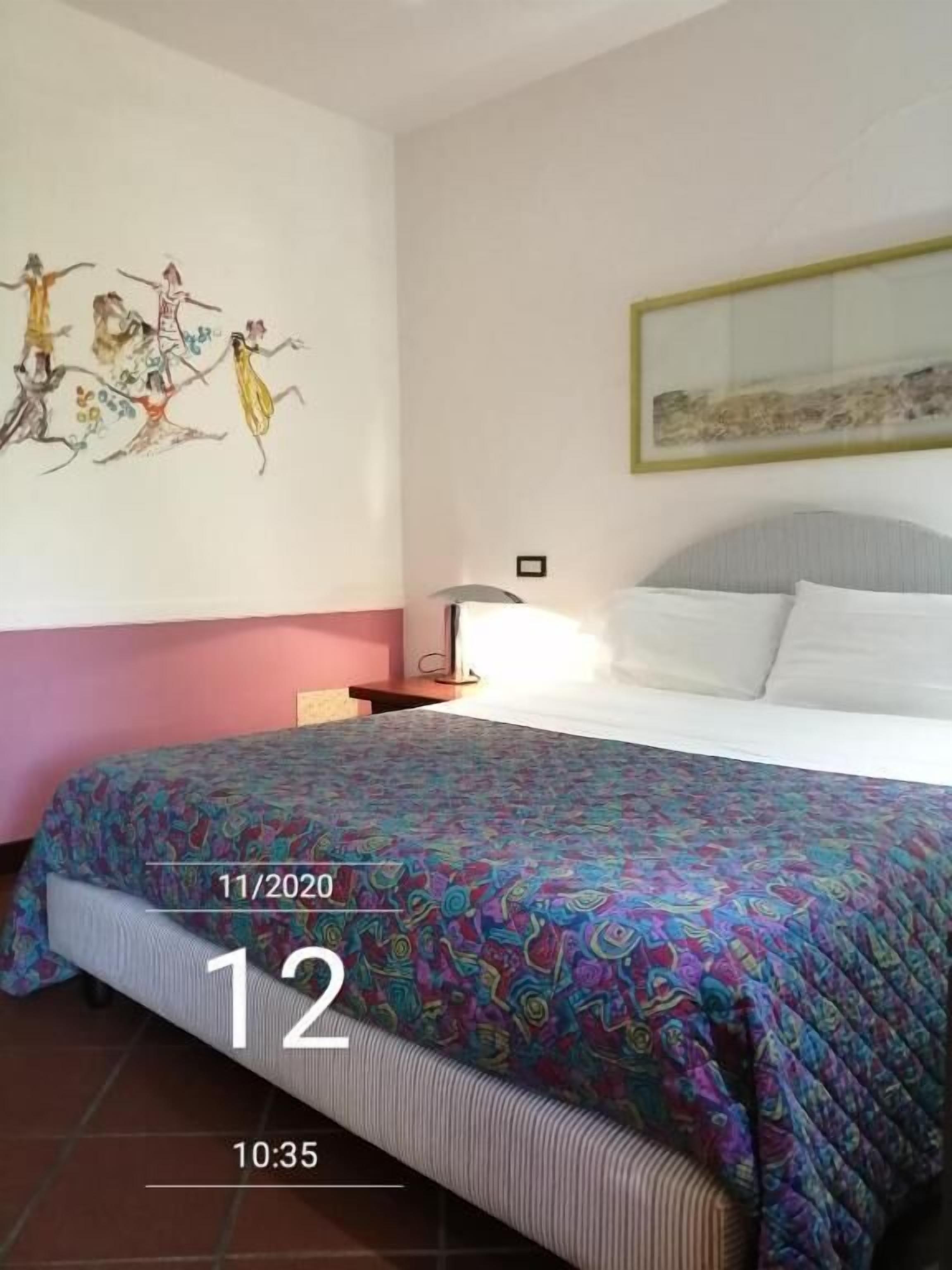Ein Hotelzimmer mit einem Bett, einem Nachttisch, einer Wanduhr und einem Gemälde.