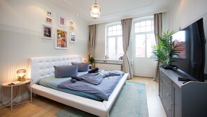 Une chambre moderne avec un grand lit, des tables de chevet, une télévision et une fenêtre avec des rideaux.