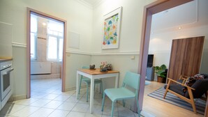 Une cuisine moderne avec des meubles blancs, un coin repas avec une table et des chaises, et un salon avec un canapé et un téléviseur.