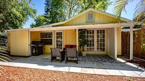 Ein gelbes Haus mit überdachter Terrasse, zwei Korbstühle, einem Grill und einem Blumentopf.