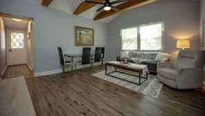 Ein geräumiges Wohnzimmer mit hohen Decken, Holzbalken, einem Deckenventilator, einer Couch, einem Couchtisch und einem Essbereich mit Stühlen.