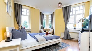 A bedroom with a bed, bedside table, lamp, and a view of the outside through large windows. - ★ Snugly Jugendstil Flat in the ❤ of Erfurt ★ (Erfurt)