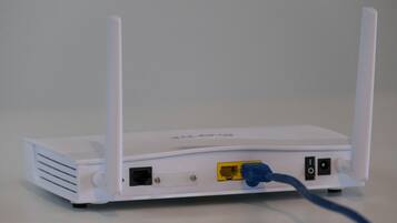 A white router with two antennas, a yellow Ethernet port, and a blue Ethernet cable plugged in.