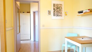 A hallway leading to a room with a wooden table and a light blue chair, a framed picture on the wall, and a bookshelf with books. - ★ Snugly Jugendstil Flat in the ❤ of Erfurt ★ (Erfurt)