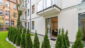 A modern building with a glass entrance, a balcony, and a row of evergreen trees in the foreground. - Climatic Studio with Terrace | 500 m to the Old Town Square (Poznan)