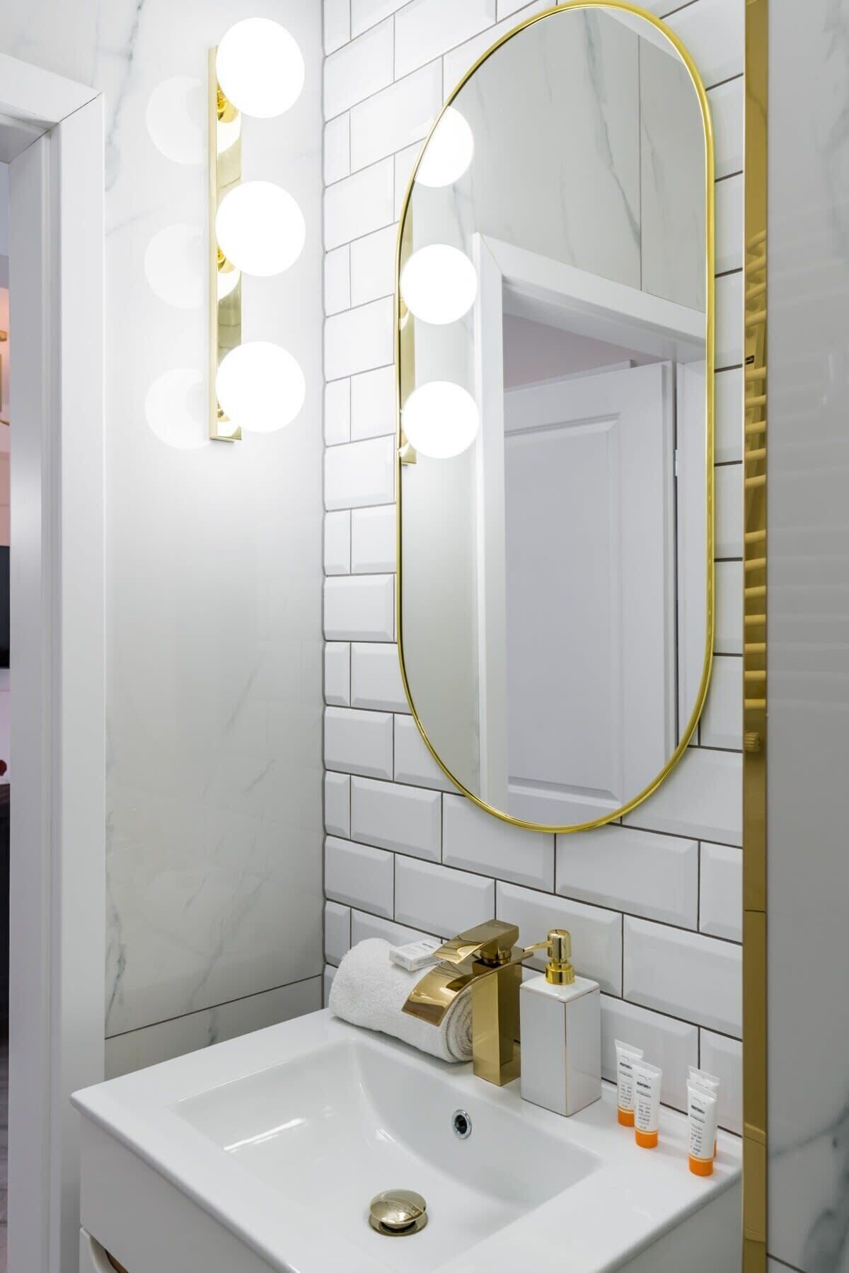 A bathroom with a white sink, gold fixtures, and a mirror with lights.