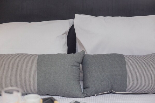 Ein Bett mit grauen und weißen Kissen, einem gestreiften Kissen und einer weißen Decke.