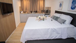 Ein Hotelzimmer mit einem großen Bett, einem Flachbildfernseher, einer Küchenzeile und einem Fenster mit Vorhängen.
