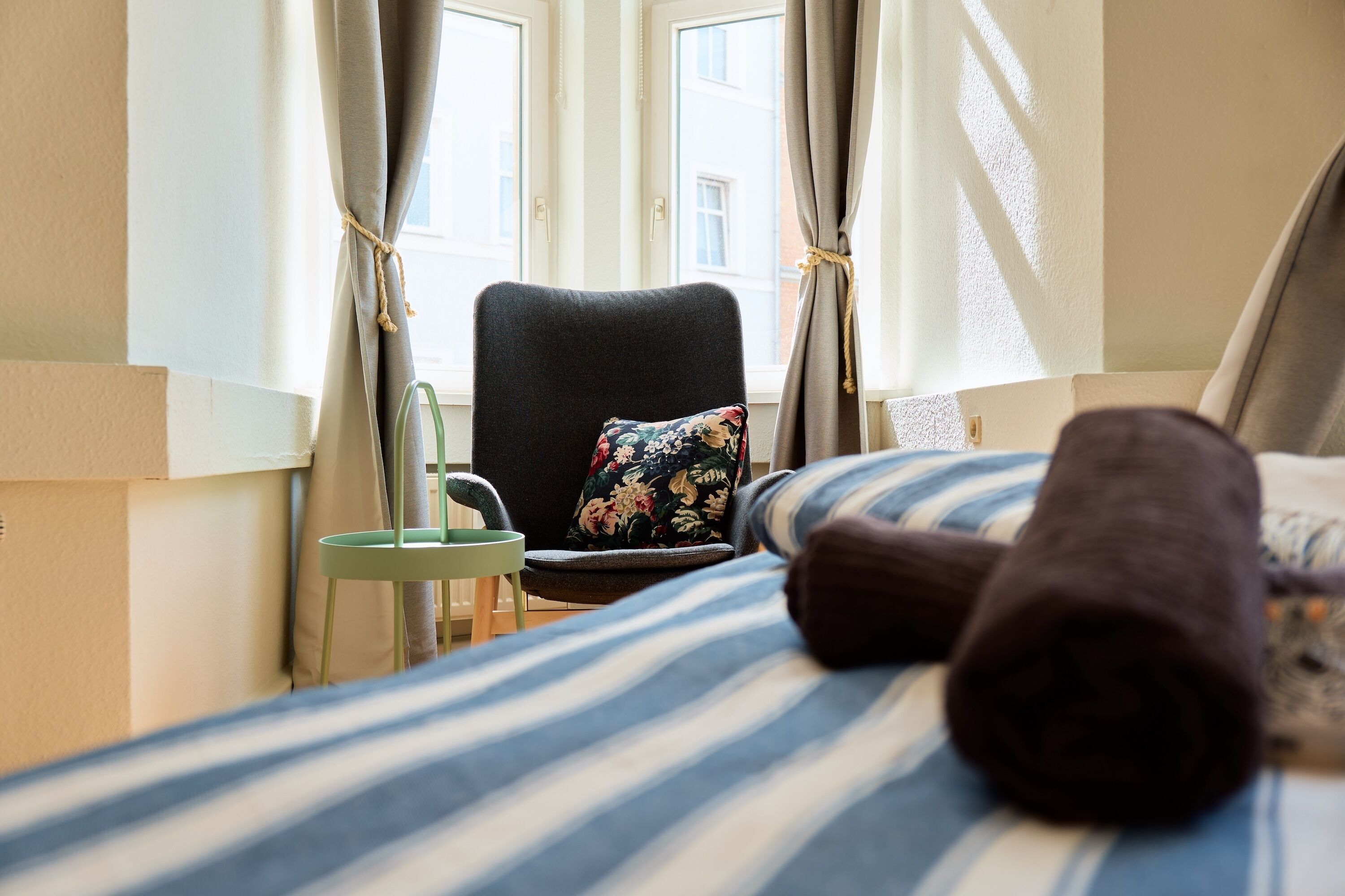 Ein Hotelzimmer mit einem Bett, einem Sessel, einem kleinen Tisch und Vorhängen.