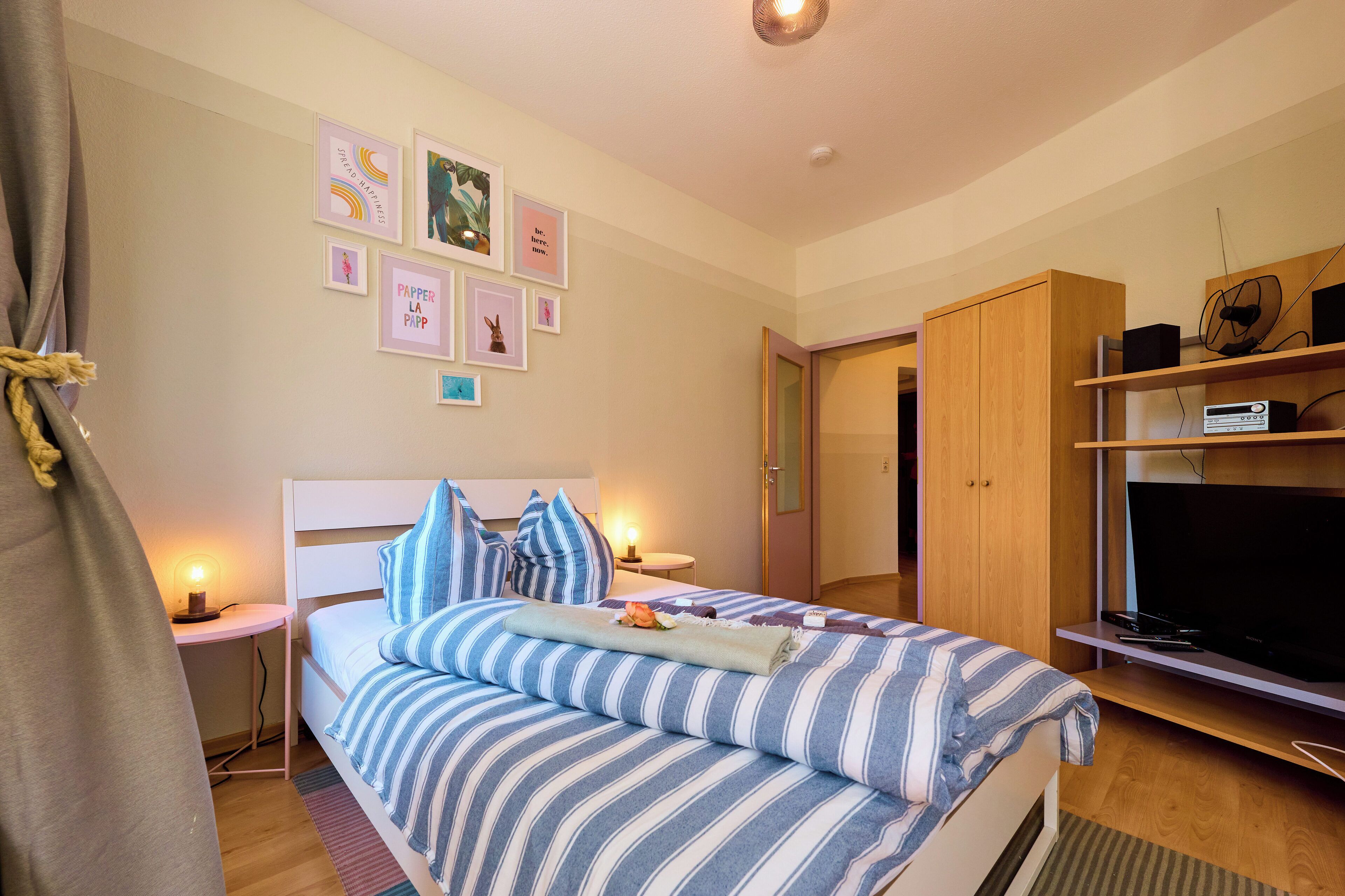 Quarto com cama, mesas de cabeceira, televisão e guarda-roupa.