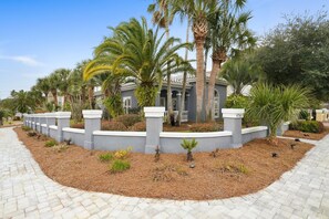 A landscaped area with a paved walkway, palm trees, and a building with columns. - TERRA PALMS: Beach cottage with community pool one block from the beach! (Destin)