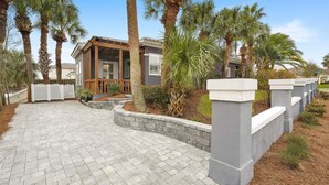 Propiedad residencial con entrada pavimentada, palmeras y una casa con porche cubierto.