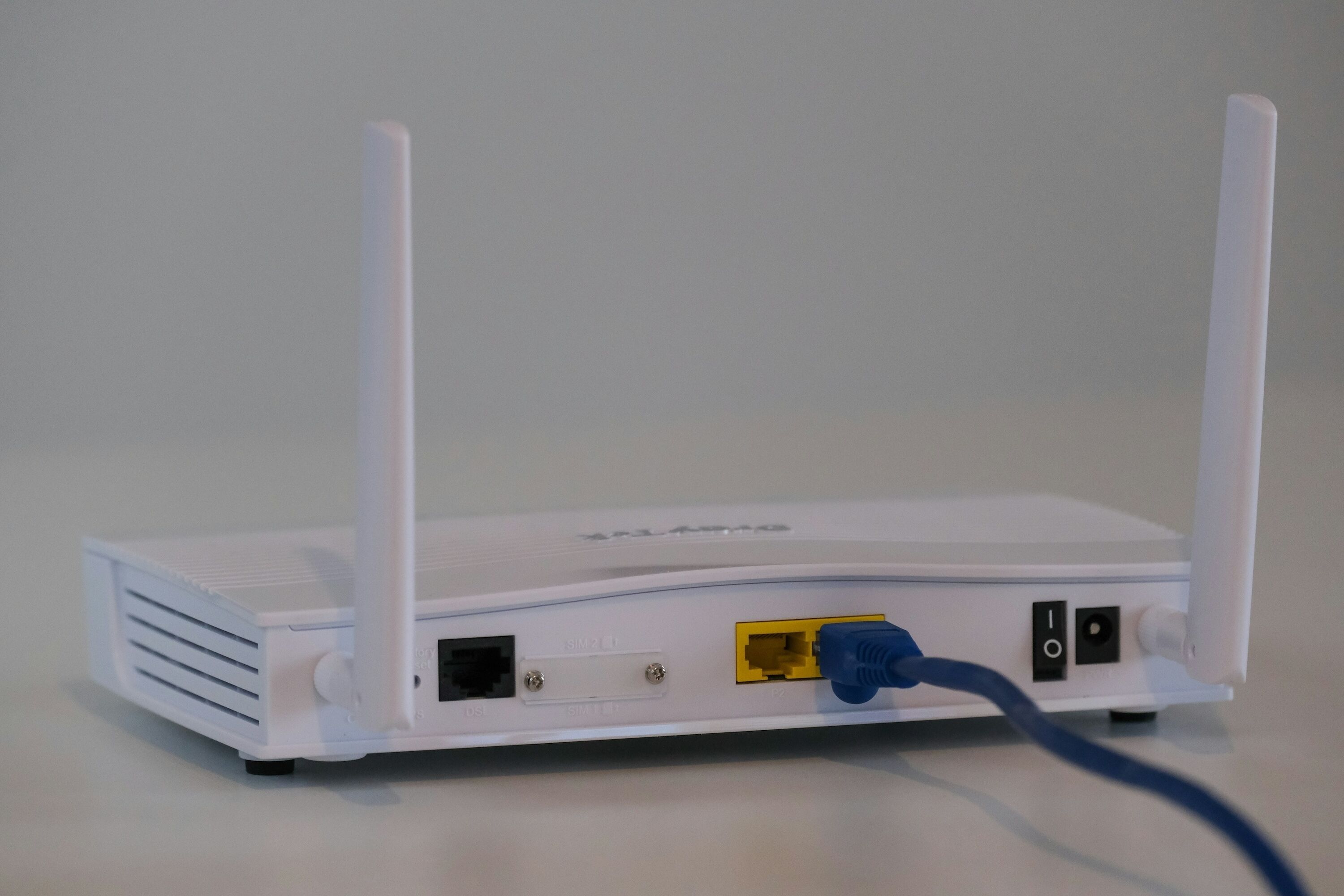 Ein weißer Router mit zwei Antennen, einem gelben Ethernet-Anschluss und einem blauen Ethernet-Kabel.