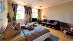 A modern bedroom with a large bed, a sofa, a TV, and a desk.
