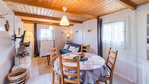 A cozy room with a wooden ceiling, a round dining table with chairs, a sofa, and a window with curtains. - Brittany, Cote de Granit Rose, Chalet with sea view, feet in the water (Trébeurden)