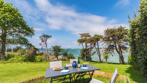 An outdoor dining area with a table set for two, overlooking a body of water and surrounded by trees. - Brittany, Cote de Granit Rose, Chalet with sea view, feet in the water (Trébeurden)