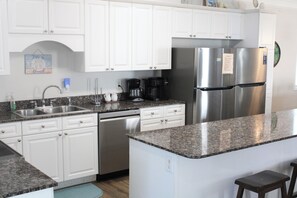Una cocina moderna con armarios blancos, electrodomésticos de acero inoxidable, encimeras de granito y una cafetera.