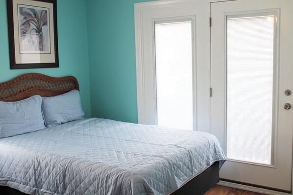 Un dormitorio con cama, cabecera y una puerta con persianas.