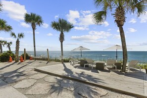 Relax on the beachside deck with lounge chairs and tables, surrounded by palm trees and the ocean.