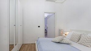 Ein Schlafzimmer mit einem Bett, einem Nachttisch und einer Nachttischlampe. Eine Tür führt in einen anderen Raum.