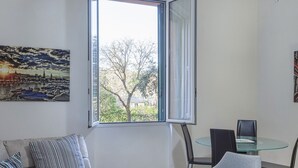 Un salon moderne avec un canapé, une table en verre et deux fauteuils. Une grande fenêtre offre une vue sur l’extérieur.