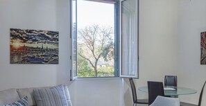 Un salon moderne avec un canapé, une table en verre et deux fauteuils. Une grande fenêtre offre une vue sur l’extérieur.