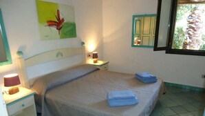Une chambre à coucher bien rangée, avec un lit, des lampes de chevet, une petite table et une fenêtre donnant sur un paysage verdoyant.