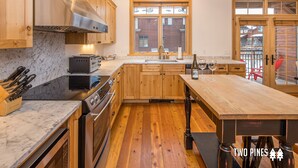 A modern kitchen with wooden cabinets, a marble countertop, and a large island. - Inviting Spanish Peaks Townhome|Private Hot Tub| 15 min Drive to Resort (Big Sky)