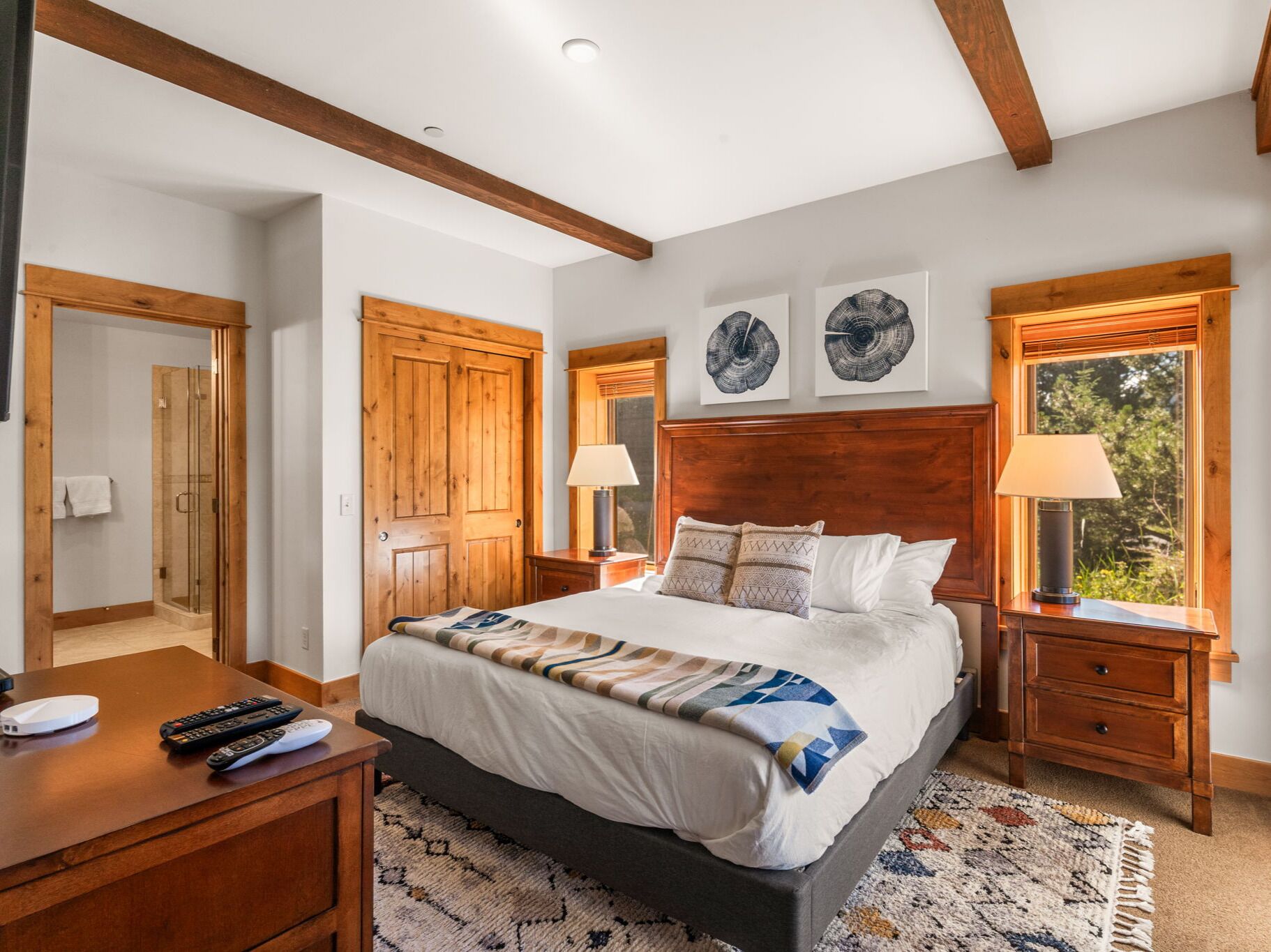 A bedroom with a large bed, wooden headboard, two bedside tables with lamps, a wooden wardrobe, and a window with a view of greenery.