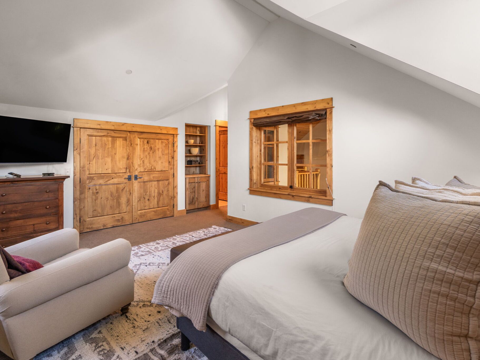 A bedroom with a bed, a TV, wooden wardrobes, and a window.