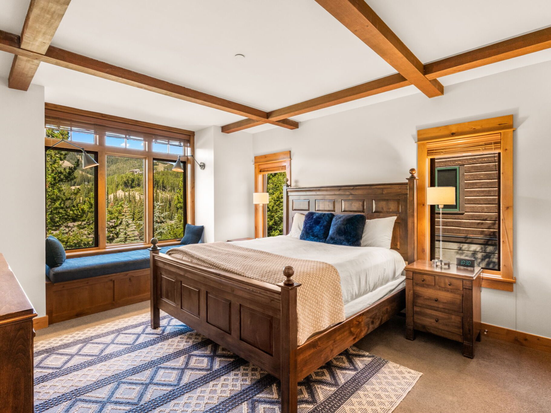 Un dormitorio con una cama de madera, un banco junto a la ventana y una mesita de noche con una lámpara.