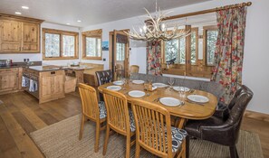 Uma sala de jantar com uma mesa de madeira posta para seis pessoas, rodeada por seis cadeiras, e uma cozinha com armários de madeira e forno embutido.