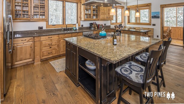 A spacious kitchen with wooden cabinets, granite countertops, and a large island with bar stools. - Gorgeous Home! Private Deck, Hot Tub, Stunning Views, 15 Min Drive to  Resort! (Big Sky)