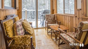 A cozy cabin interior with a wooden deck, a sofa with patterned cushions, and a table with a chessboard. - Gorgeous Home! Private Deck, Hot Tub, Stunning Views, 15 Min Drive to  Resort! (Big Sky)