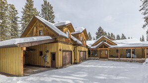 A large wooden lodge with multiple garage doors and a covered driveway. - Gorgeous Home! Private Deck, Hot Tub, Stunning Views, 15 Min Drive to  Resort! (Big Sky)