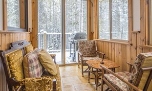 A cozy cabin interior with a wooden deck, a sofa with patterned cushions, and a table with a chessboard.