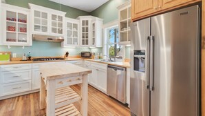 Une cuisine moderne avec des meubles blancs, des appareils en acier inoxydable et une table en bois.