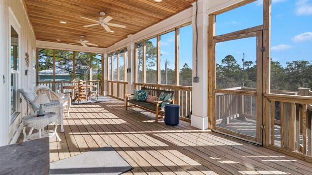 Un espace extérieur abrité doté d’un plancher en bois, d’un banc en bois avec des coussins et d’un ventilateur de plafond.