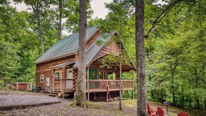 Une cabane dotée d’un porche et de chaises rouges, entourée d’arbres.