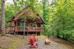 A wooden cabin with a deck, surrounded by trees.