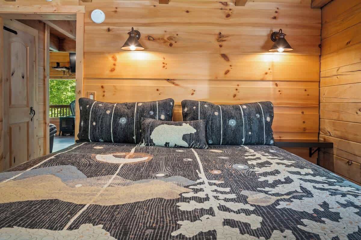 Interior de una cabaña de madera con una cama que tiene un edredón estampado y un diseño de almohada original.